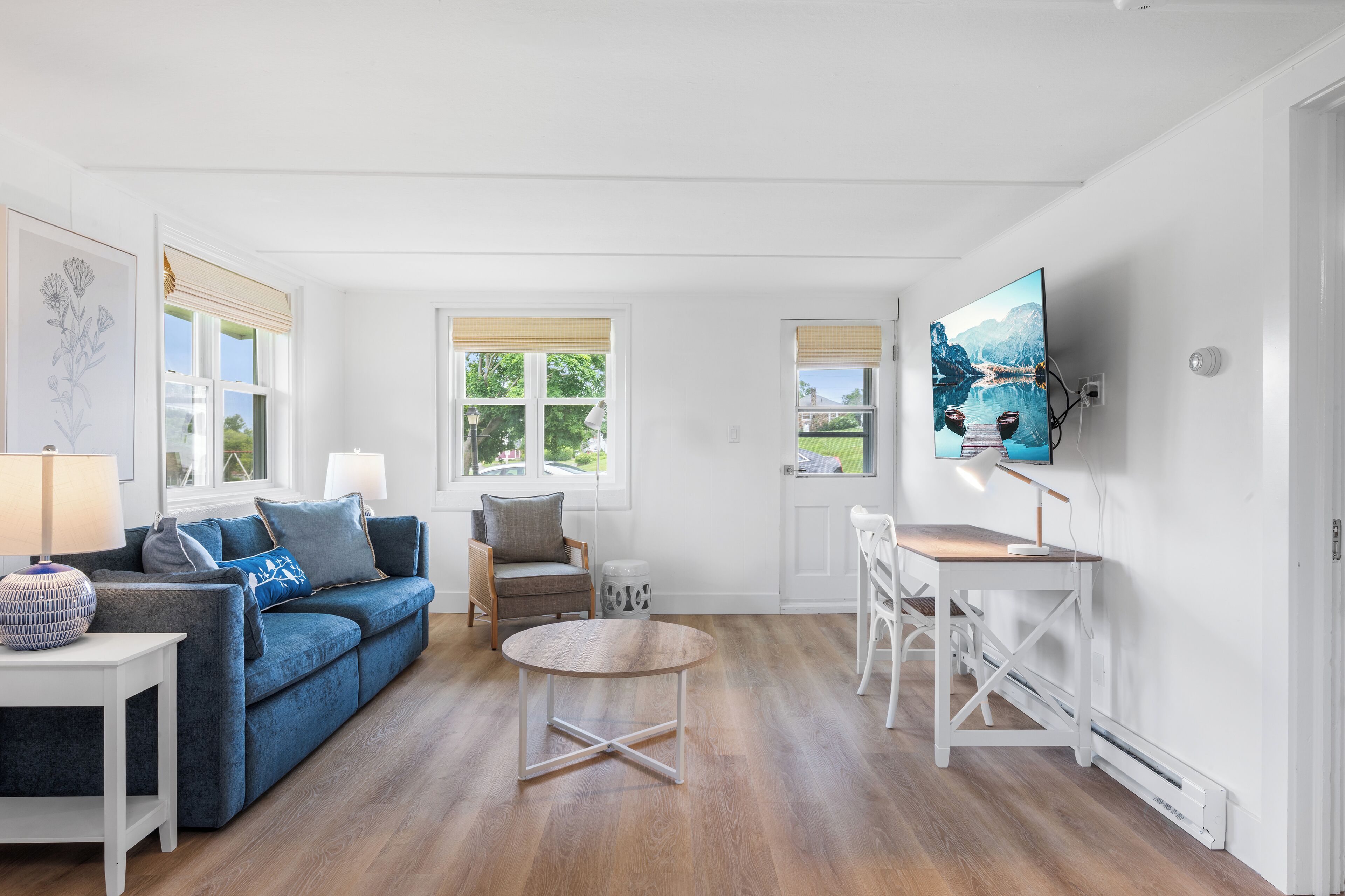 Un salon moderne avec un canapé bleu, une table basse ronde et un téléviseur blanc fixé au mur.