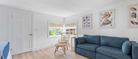 A spacious living room with a blue sofa, a dining area with wicker chairs, and framed artwork on the walls.