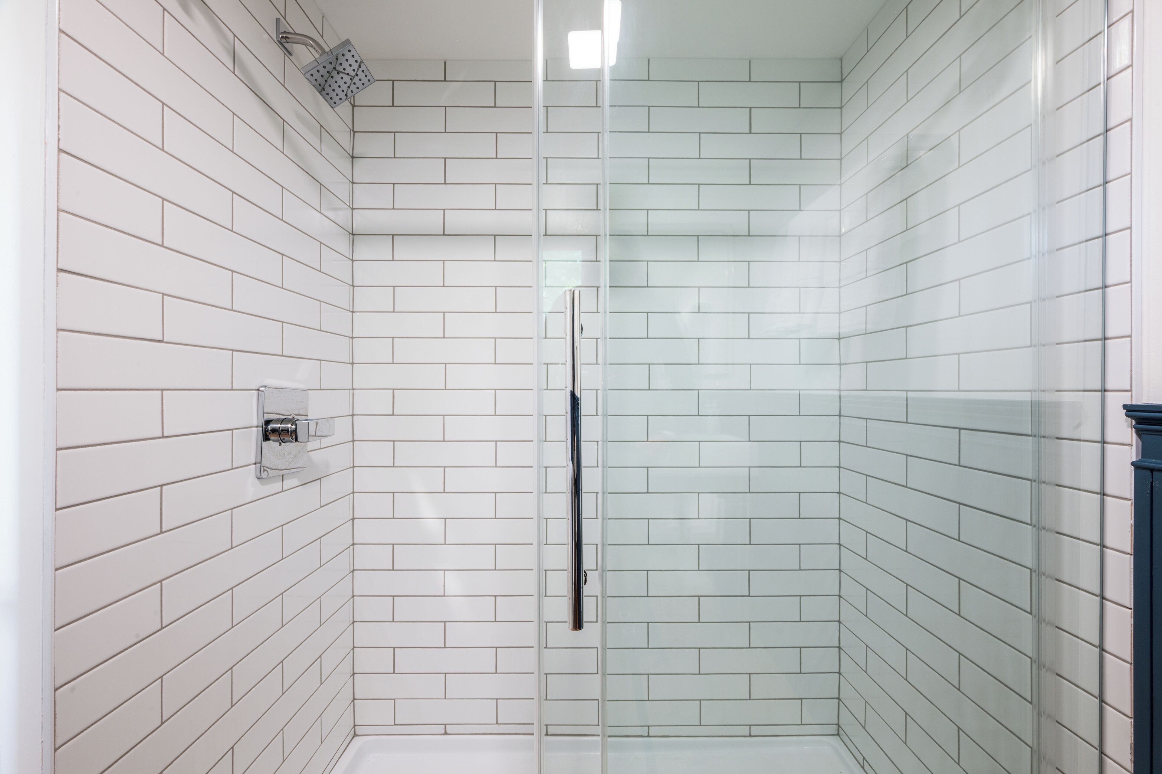 A modern bathroom with white subway tiles, a glass shower enclosure, and a visible electrical outlet on the wall.