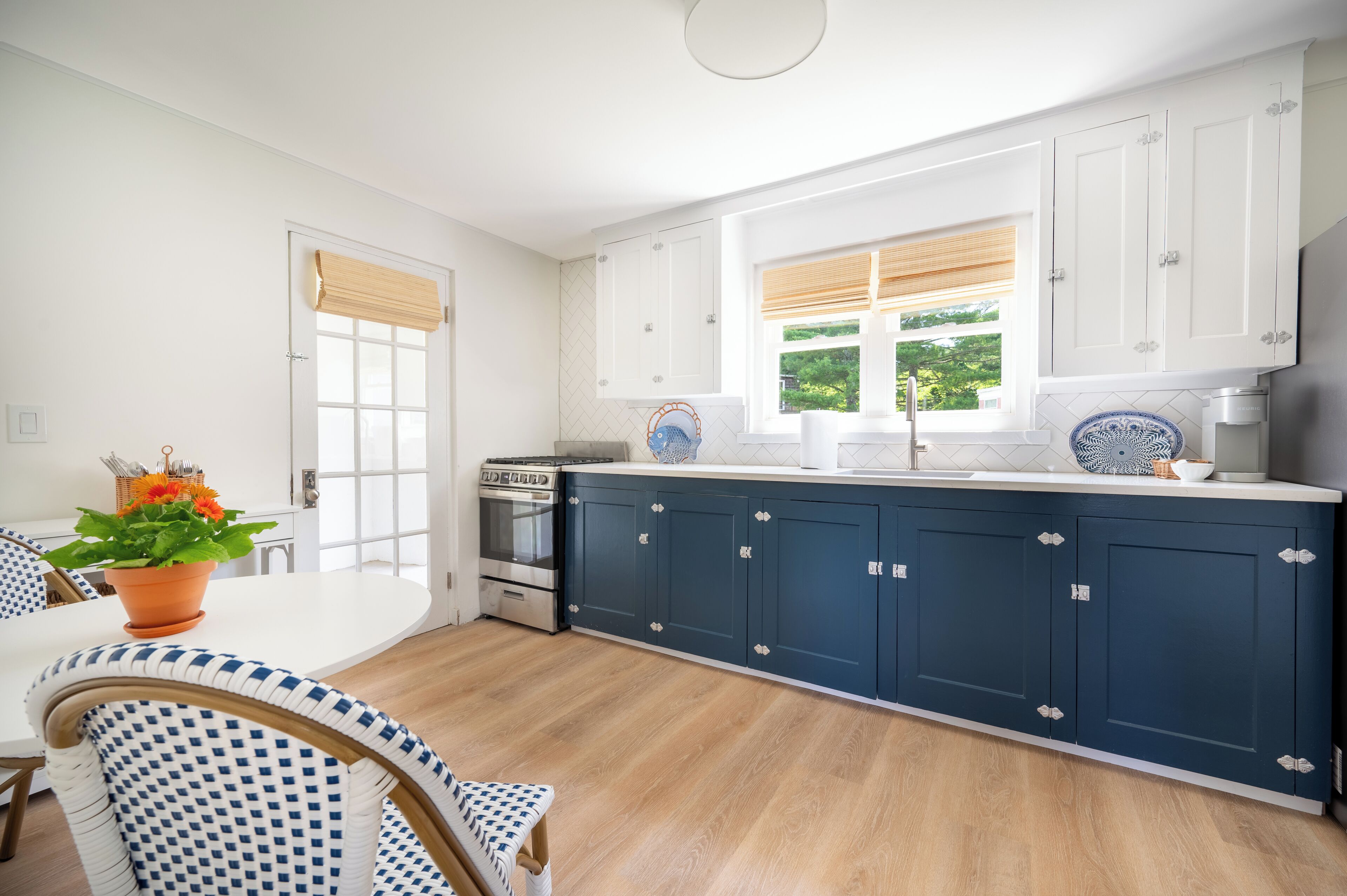 A modern kitchen with white cabinets, a blue countertop, and a window with blinds.