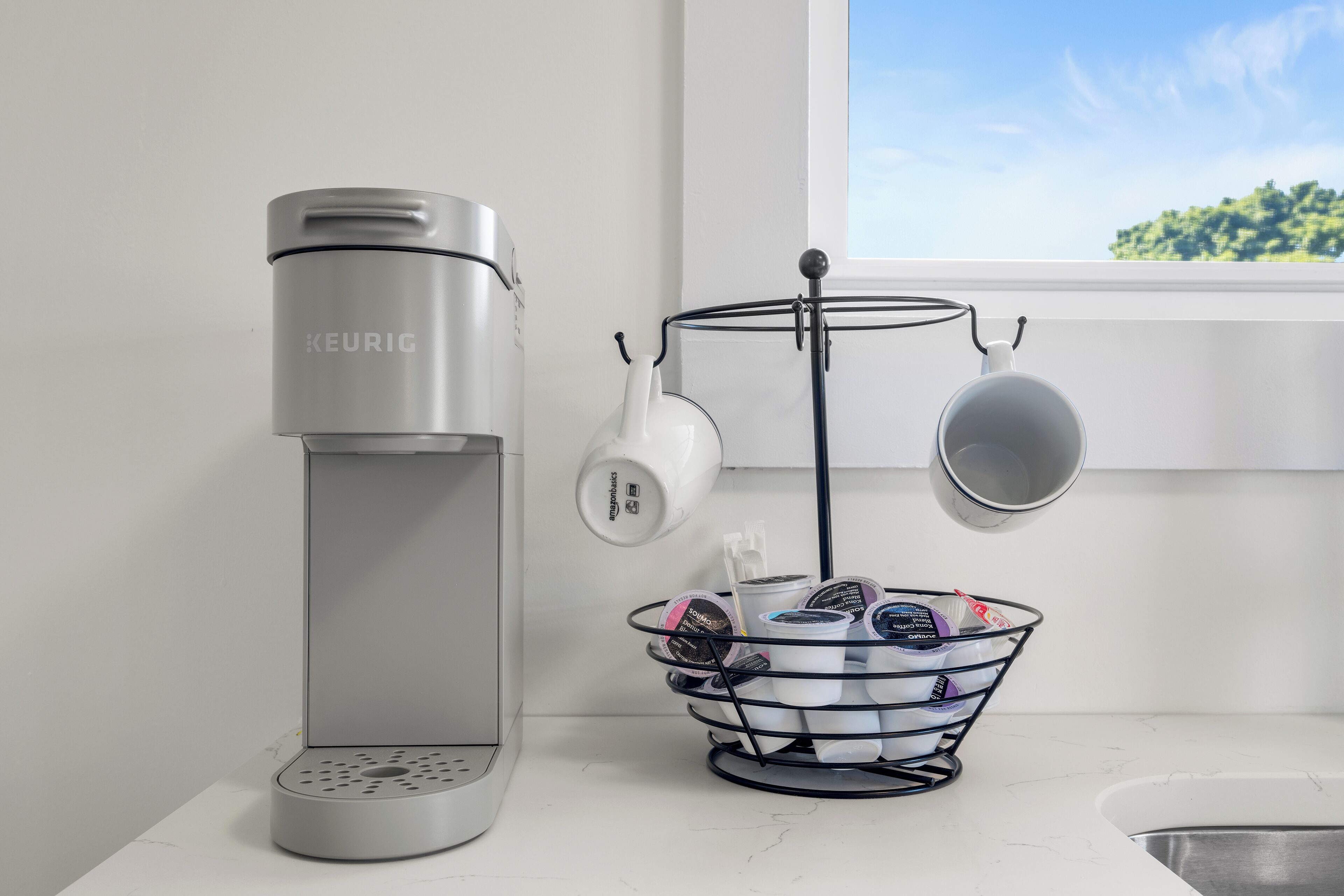 Una cafetera Keurig, una taza de café y un portavasos sobre una encimera cerca de una ventana.