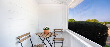 A small balcony with white paneled walls, a wooden table with a potted plant, and two wooden chairs.