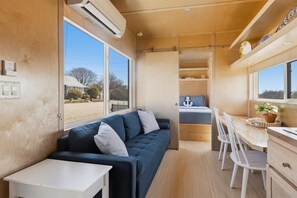 Ein kompakter Wohnbereich mit Sofa, Esstisch, Stühlen und einer kleinen Küchenzeile.