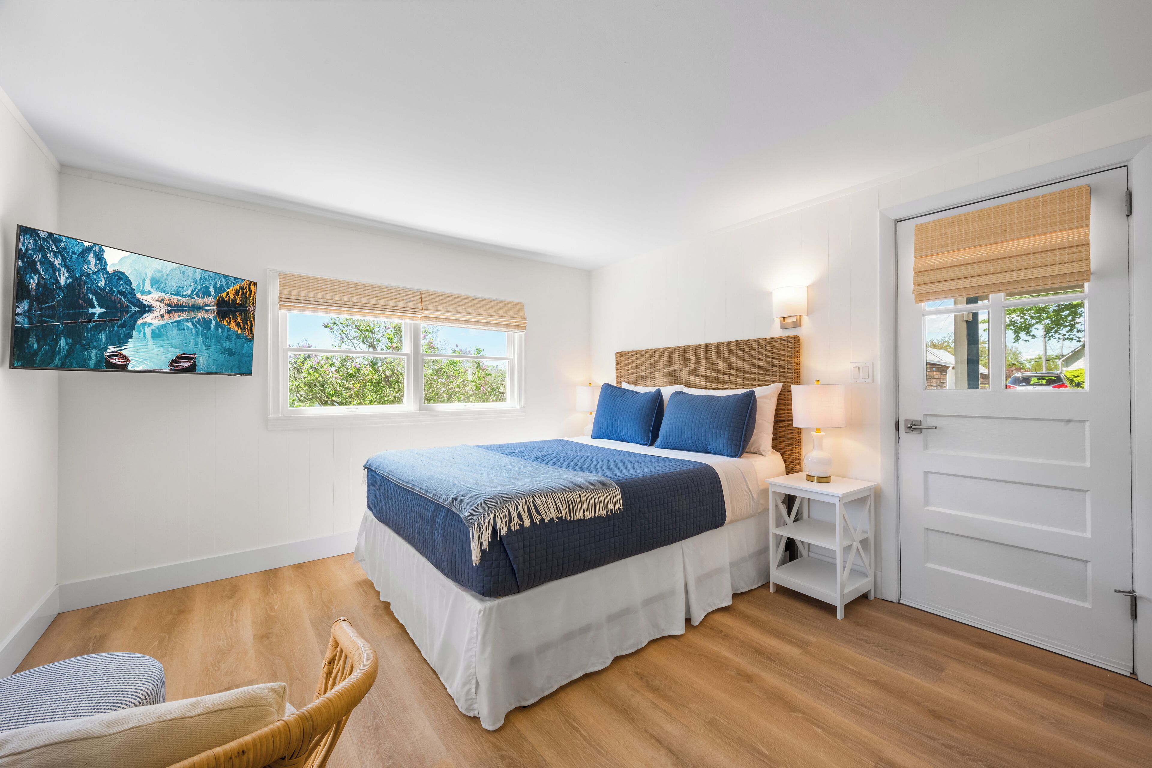 Un dormitorio con cama, una silla, una mesita de noche, una lámpara, un cuadro y una puerta.