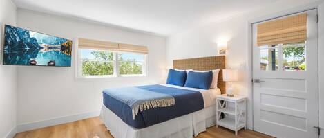 Un dormitorio con cama, una silla, una mesita de noche, una lámpara, un cuadro y una puerta.