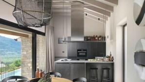 A modern kitchen with a central island, dark cabinetry, and a view of a mountainous landscape.