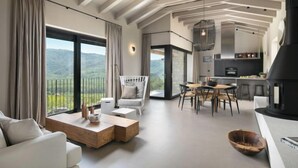 A modern living room with a large window, a dining area, and a kitchen with a built-in stove.