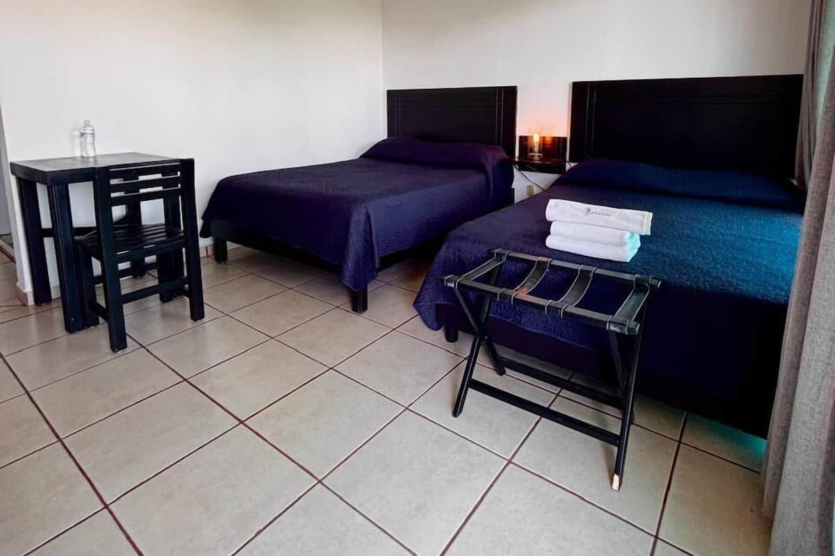 Habitación de hotel con dos camas, una mesita, una silla y un tendedero.