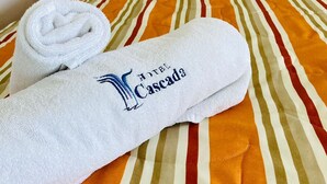 A neatly folded towel with a hotel logo on a bed with striped bedding. - HOTEL CASCADA (Cuautla)