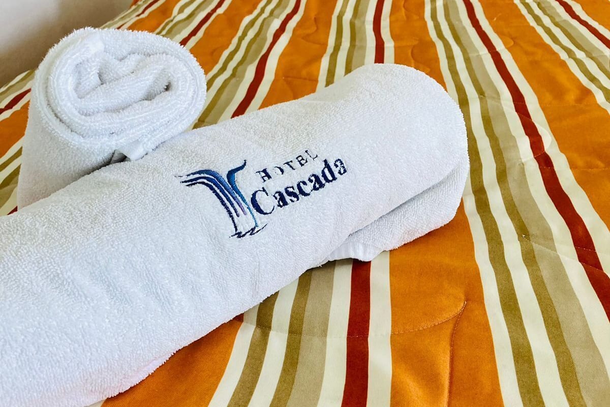 Una toalla doblada con el logo de un hotel sobre una cama con ropa de cama a rayas.