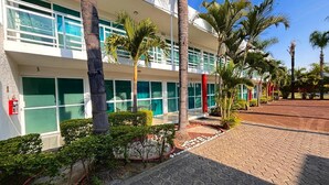 A hotel with a modern design, featuring a flat roof, large windows, and a paved walkway with palm trees. - HOTEL CASCADA (Cuautla)