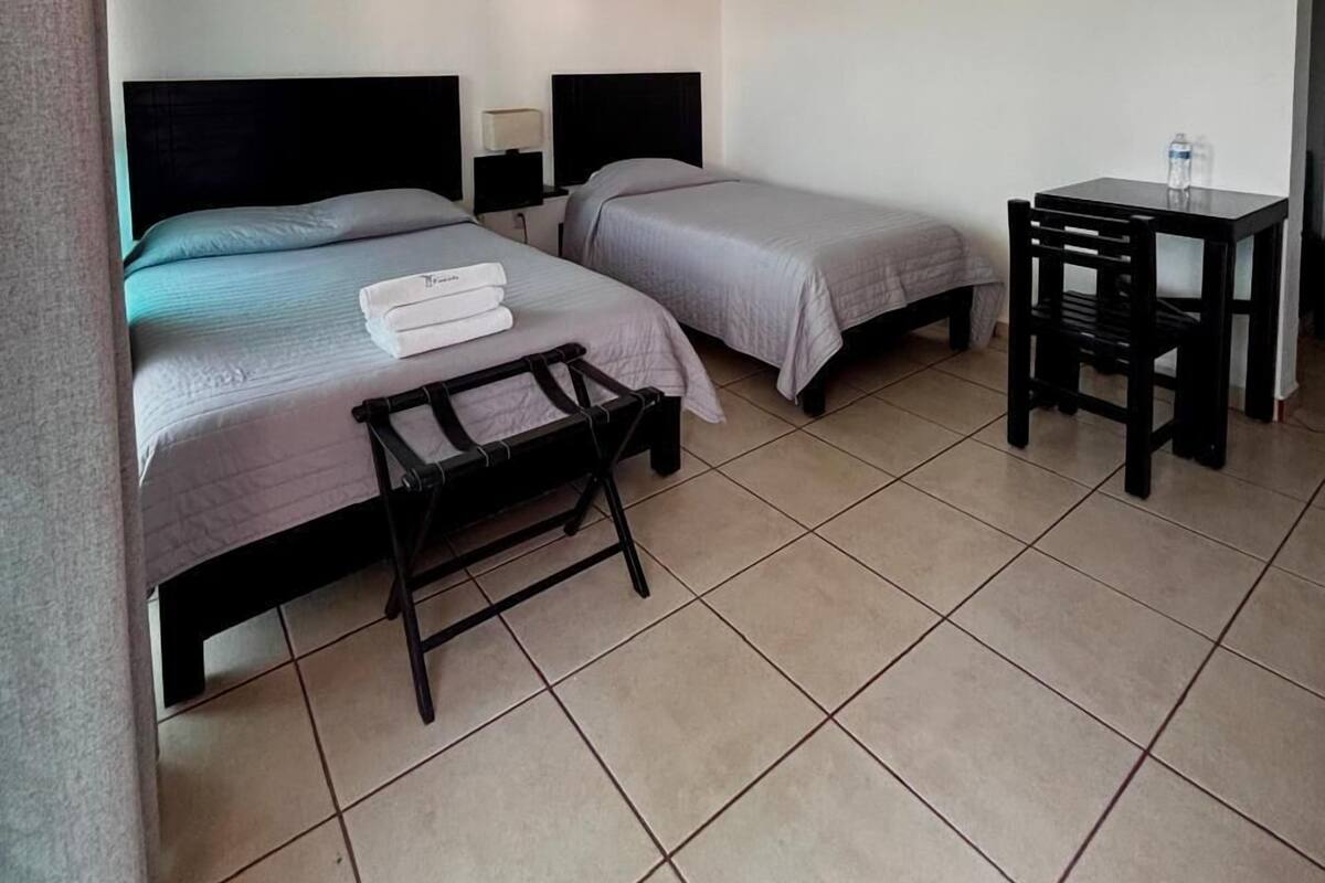 Una habitación de hotel con dos camas, un escritorio, una silla y aire acondicionado.