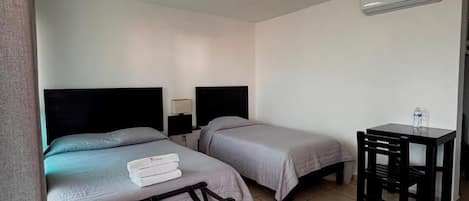 Una habitación de hotel con dos camas, un escritorio, una silla y aire acondicionado.