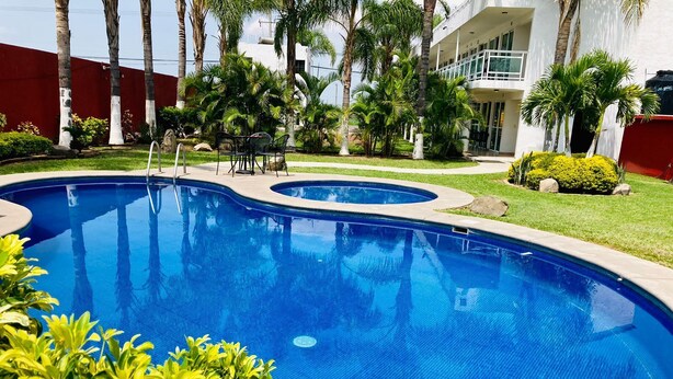 A swimming pool with a curved design, surrounded by palm trees and a well-maintained lawn. - HOTEL CASCADA (Cuautla)