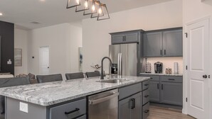A modern kitchen with grey cabinets, a stainless steel refrigerator, and a marble countertop. - Newly Built Home w/ Fresh Design! (Columbia)