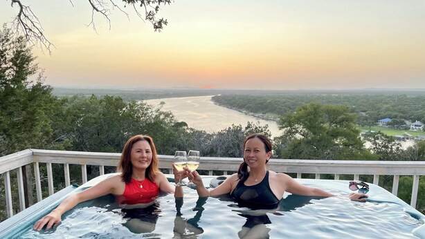 Dos personas en un jacuzzi con una vista panorámica de un río y árboles.