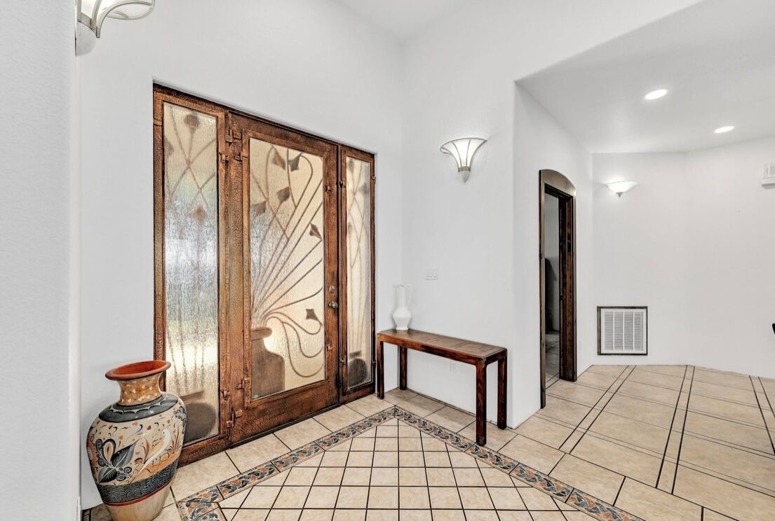 Un pasillo con suelo de baldosas, un banco de madera, un jarrón decorativo y una lámpara de pared.