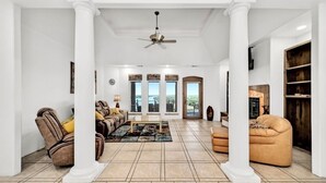 Un salón amplio con un sofá grande, una mesa de centro y una chimenea. Hay ventanas amplias y vistas al exterior.
