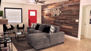 A living room with a grey sectional sofa, two black chairs, a coffee table, a red door, and a wooden wall with decorative plates. - Bradenton Cozy Haven - Escape to our charming 3-bed, 2-bath Bradenton retreat! (Bradenton)