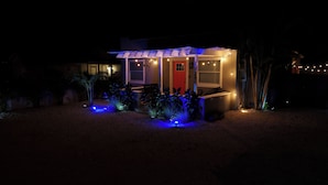 A small, modern house with a red door and a covered porch, surrounded by landscaped garden beds and illuminated by string lights. - Bradenton Cozy Haven - Escape to our charming 3-bed, 2-bath Bradenton retreat! (Bradenton)