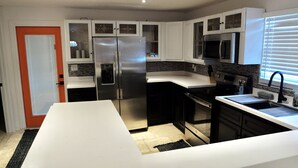 A modern kitchen with white cabinets, stainless steel appliances, and a black countertop. - Bradenton Cozy Haven - Escape to our charming 3-bed, 2-bath Bradenton retreat! (Bradenton)