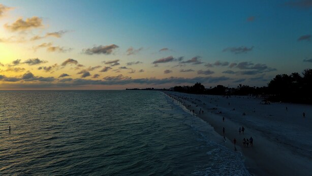 A beach with people walking along the shore and a sunset in the background. - Bradenton Cozy Haven - Escape to our charming 3-bed, 2-bath Bradenton retreat! (Bradenton)