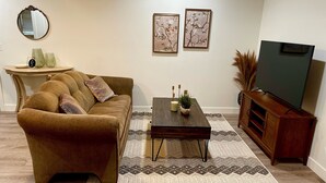 A living room with a brown sofa, a coffee table, a TV stand, and a patterned rug. - Cozy One Bedroom Apartment in Sheridan (Sheridan)