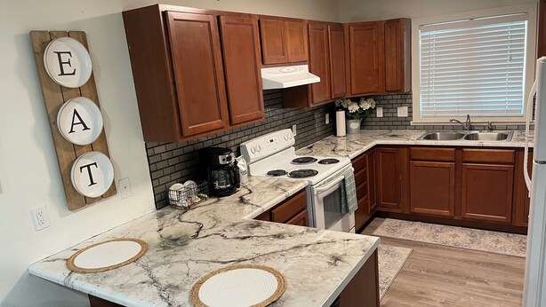 A modern kitchen with wooden cabinets, a white stove, and a marble countertop. - Cozy One Bedroom Apartment in Sheridan (Sheridan)