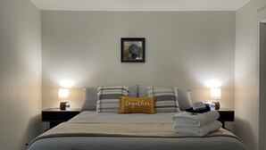 A neatly made bed with a striped pillow and a 'better together' pillow, two bedside lamps, a framed picture on the wall, and a folded towel on the bed. - Cozy One Bedroom Apartment in Sheridan (Sheridan)