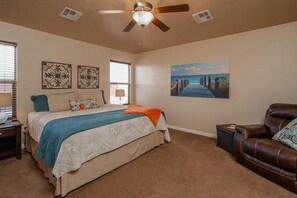Relax in this serene bedroom with a large bed, ceiling fan, and a cozy armchair.