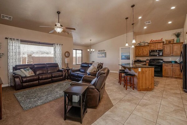 Relax in the spacious living area with a sofa set and matching ottoman, adjacent to a fully equipped kitchen with a refrigerator and sink.