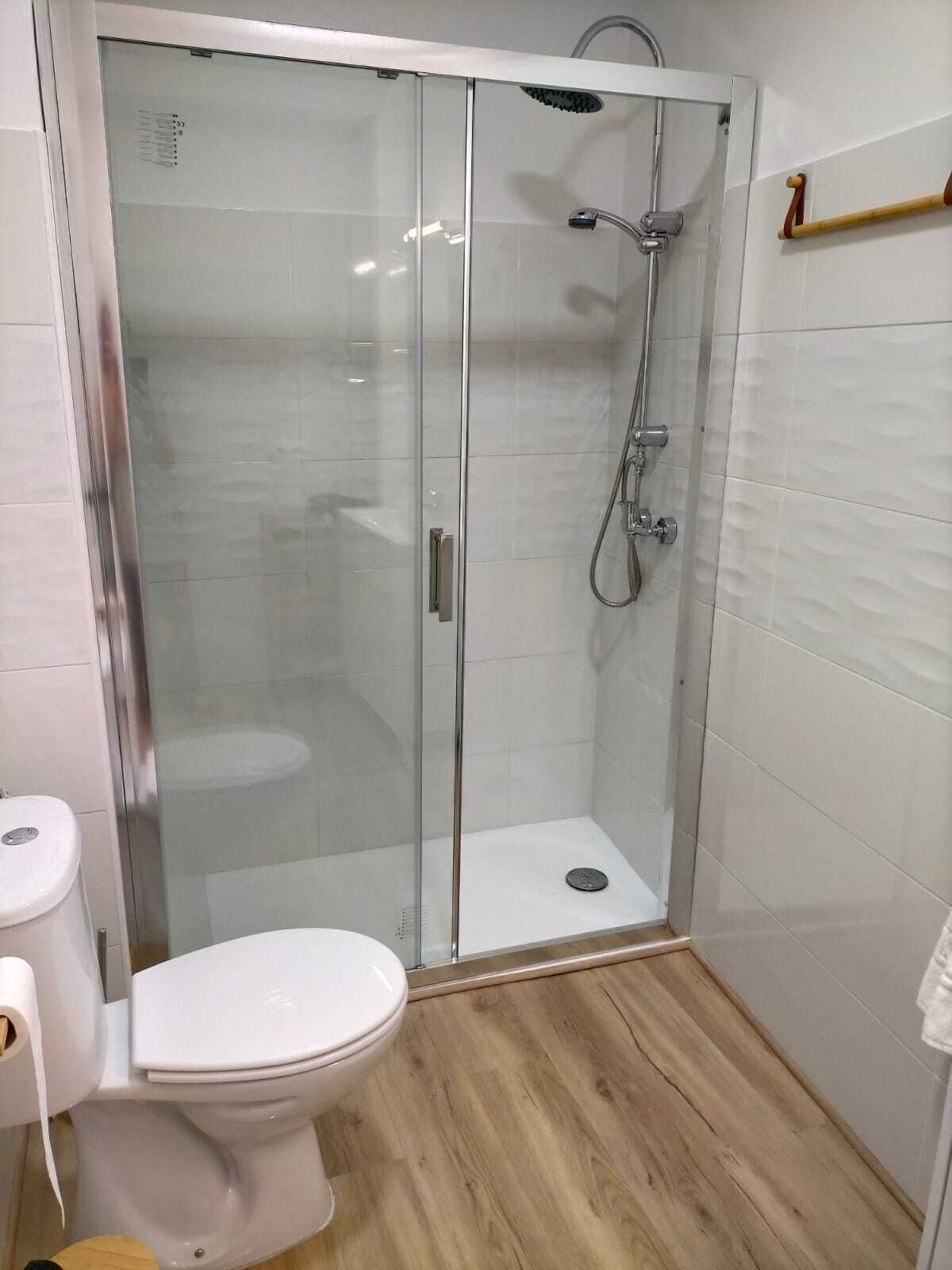Un baño moderno con ducha envuelta en vidrio, inodoro blanco y suelo de madera.