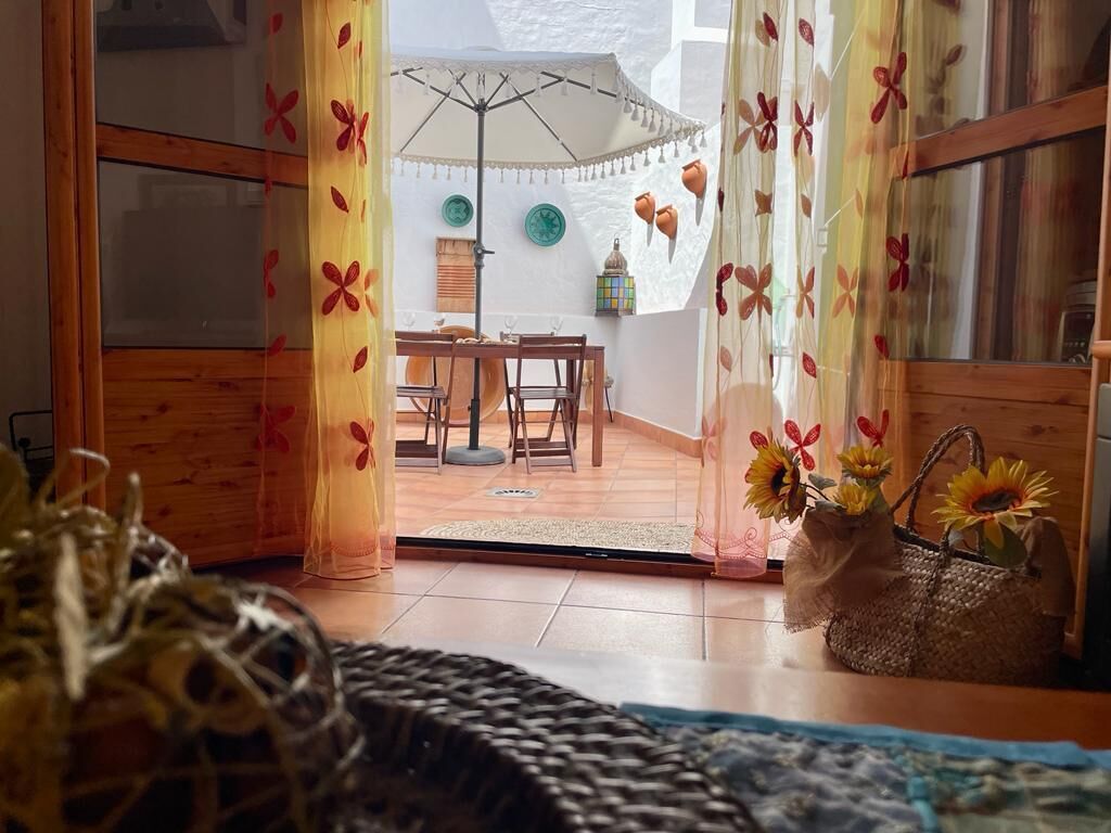 A room with a wooden floor, a dining table with chairs, a white umbrella, and a basket with sunflowers.
