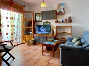 Una sala de estar con una televisión, un sofá, una mesa de madera y una silla.
