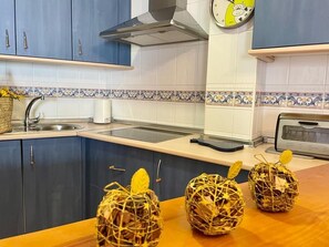 A kitchen with blue cabinets, a stainless steel sink, and a microwave. There are three decorative baskets on the counter.