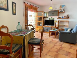Un salon comprenant un canapé, un téléviseur, un meuble en bois et une table à manger avec des chaises.