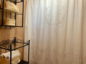 Un baño con cortina de ducha de bordado floral, un perchero metálico con toallas y una pared con azulejos.