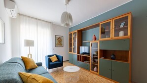 Un salon comprenant un canapé, un fauteuil bleu, une table basse et un meuble en bois avec des étagères.