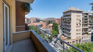 Un balcon offrant une vue sur le paysage urbain, avec des immeubles de plusieurs étages et des voitures garées.
