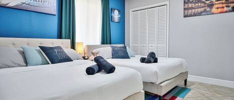 Habitación de hotel con dos camas, una ventana con cortinas, un cuadro en la pared y suelo de baldosas.