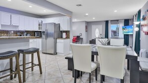 Cozinha moderna com armários brancos, geladeira de aço inoxidável e um espaço de refeições com mesa e cadeiras.