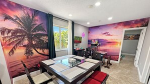 Uma sala de jantar com uma mesa de vidro, cadeiras acolchoadas e um mural com um pôr do sol.