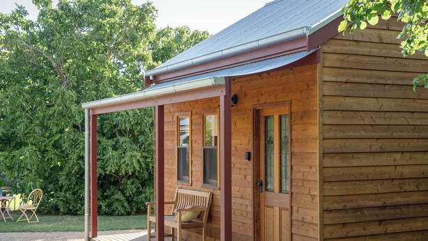 Une cabane en bois dotée d’un porche couvert, d’une porte et d’une petite fenêtre.