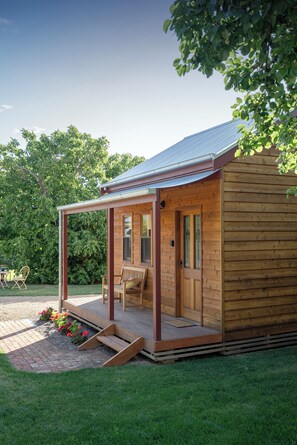 A wooden cabin with a covered porch, a door, and a small window. - Tread Lightly Cabins (Willunga)
