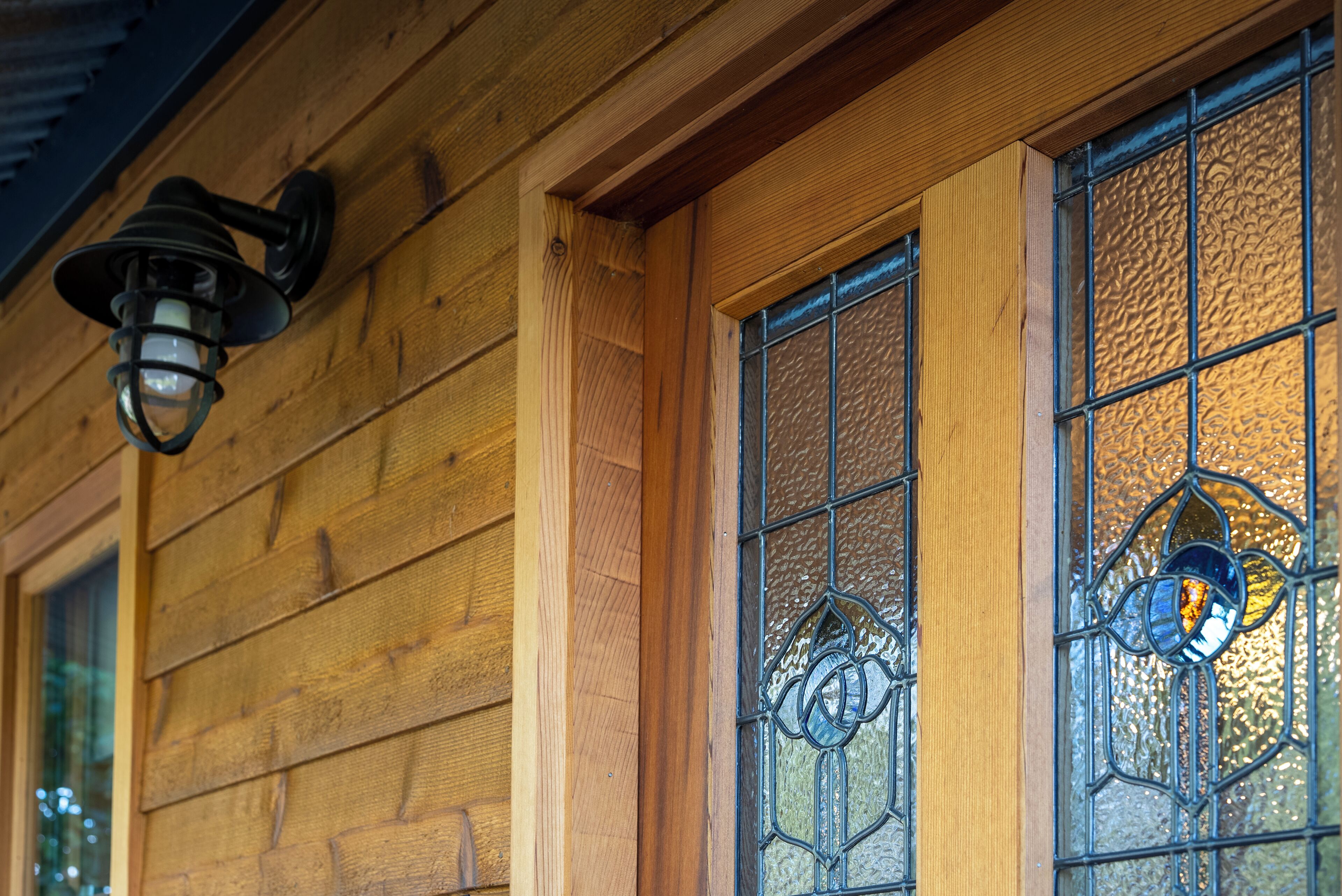A wooden building with a window featuring decorative glass and a wall-mounted light fixture.