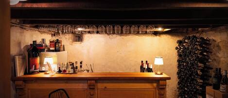 A bar area with a wooden counter, bottles, glasses, and a wine rack.