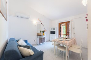 A living room with a blue sofa, a dining table set for two, and a kitchen area with a TV and cabinets.