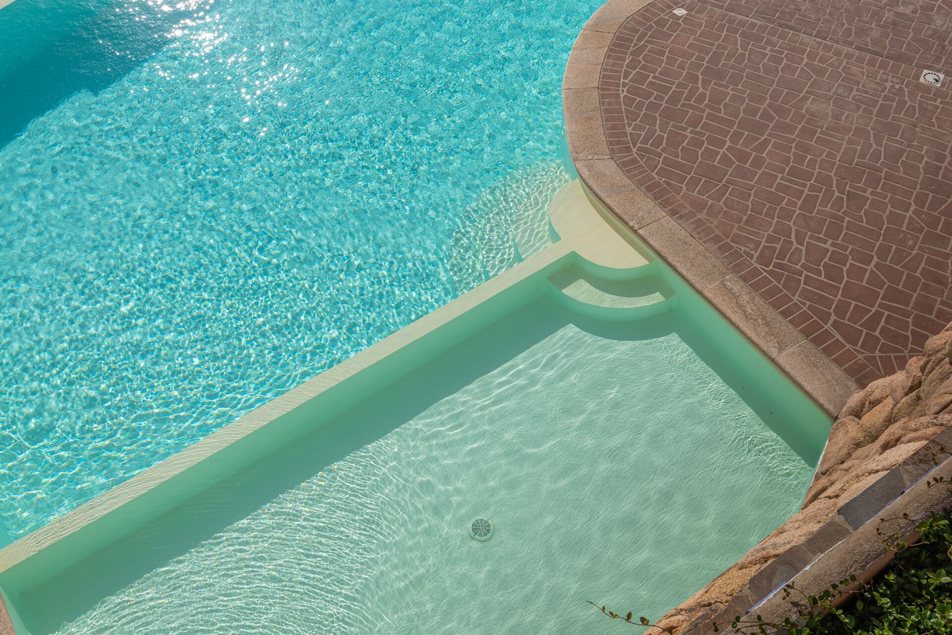 Ein klares, blaues Schwimmbecken mit einer gefliesten Kante und einer steinernen Terrasse darum.