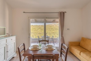 A dining area with a table set for two, a sofa, and a balcony with a view. - Elegant Residence Ea Bianca 1 Bedroom Sleeps 4 Child num0607 (Sardegna)