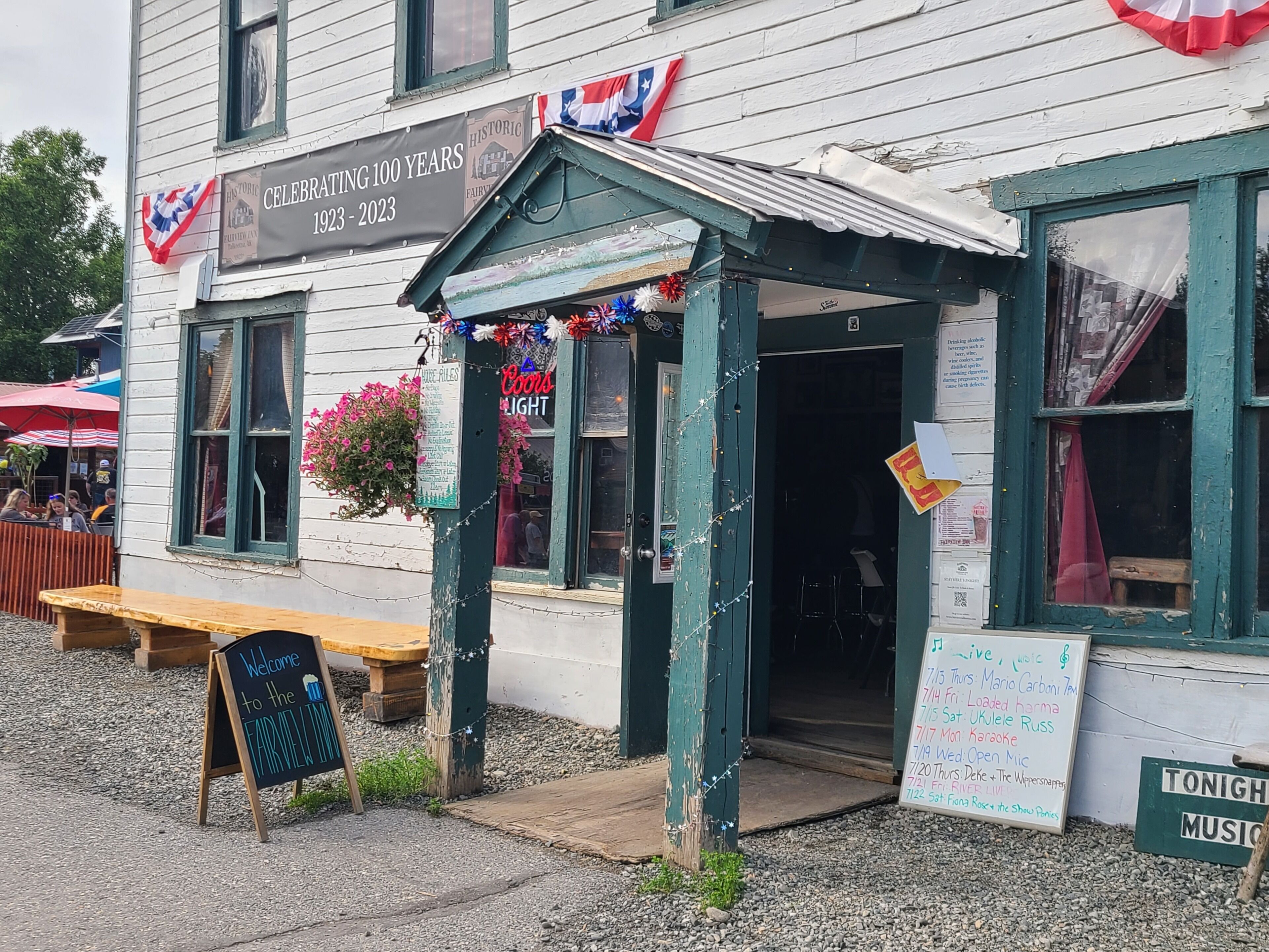 A historic building with a sign celebrating 100 years, outdoor seating, and a signboard for live music events.